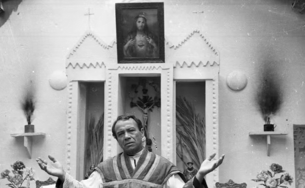 Cena da novela Padre Cicero - um padre dentro da igreja com as mãos para cima e um semblante aflito