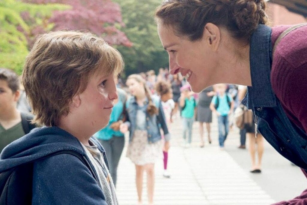 Auggie do filme "Extraordinário" e sua mãe agachados na rua olhando um para o outro