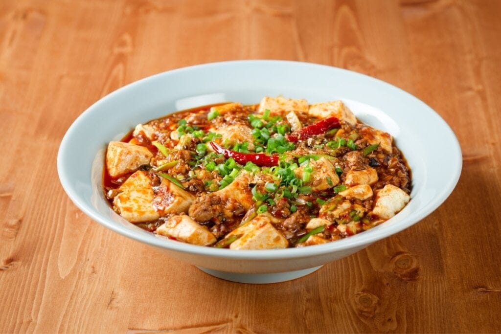 Prato branco com Mapo tofu em cima de uma mesa de madeira