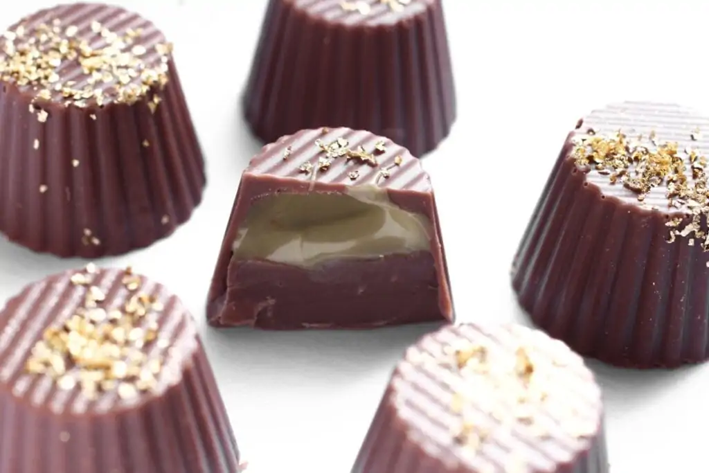 Bombons de chocolate com um recheio cremoso de pistache, finalizados com folhas douradas; um deles está cortado