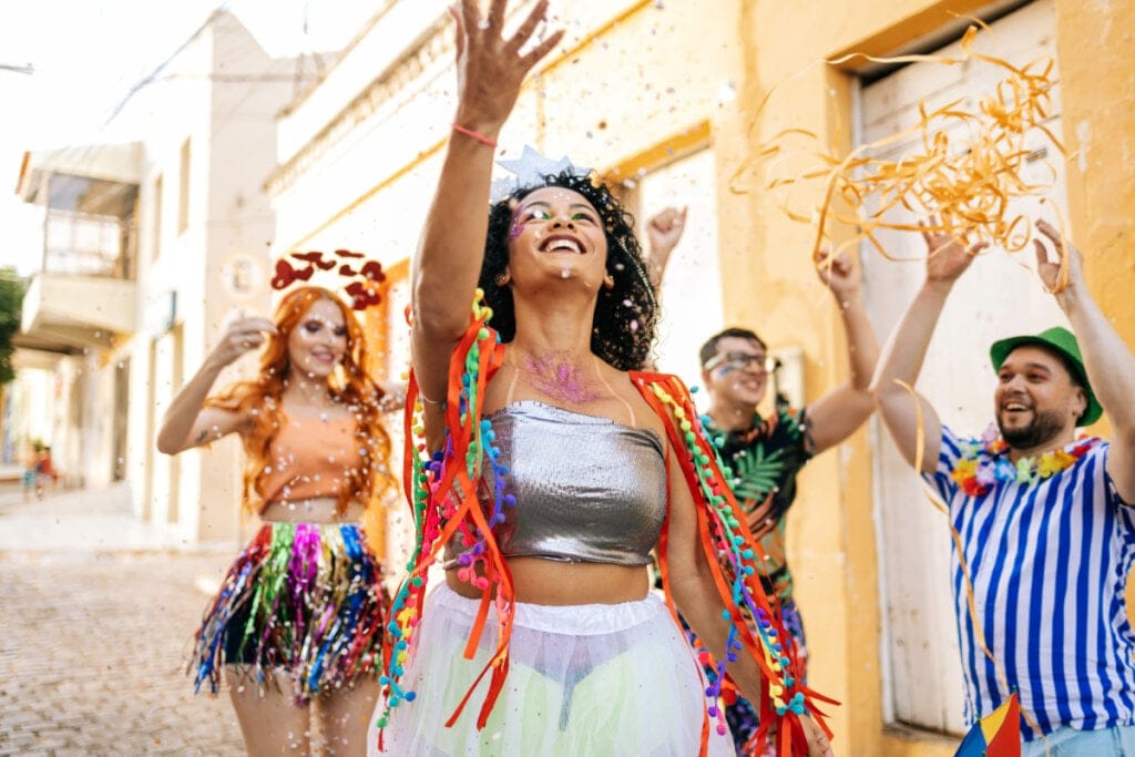 pessoas na rua, com roupa colorida e jogando confete para cima