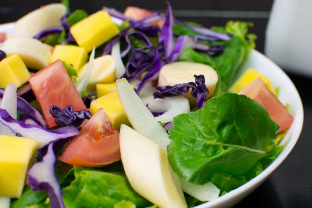 pote branco com salada com tomate, repolho roxo, maçã, manga e folhas verdes
