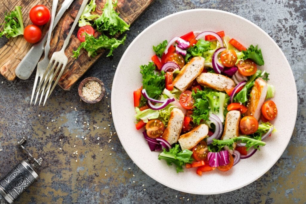 Prato branco com alface, frango, repolho, cebola, tomate, pimentão e gergelim