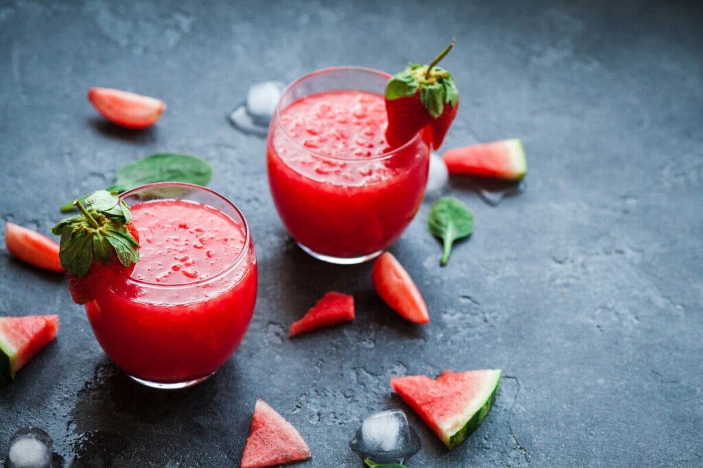 Copo de vidro com suco de melancia e morango, decorado com pedaços de morango em cima de uma mesa