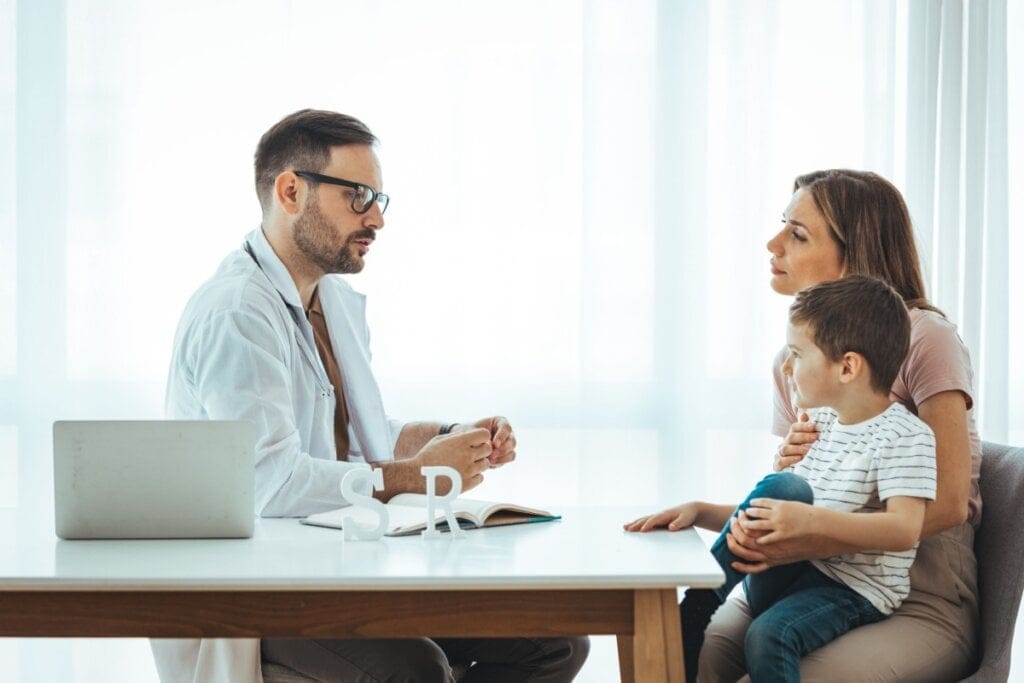Mulher e menino sentados em um consultório conversando com um médico 