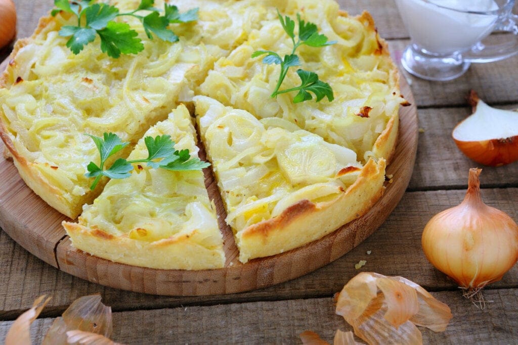 Quiche de cebola em cima de uma tábua de madeira decorada com coentro