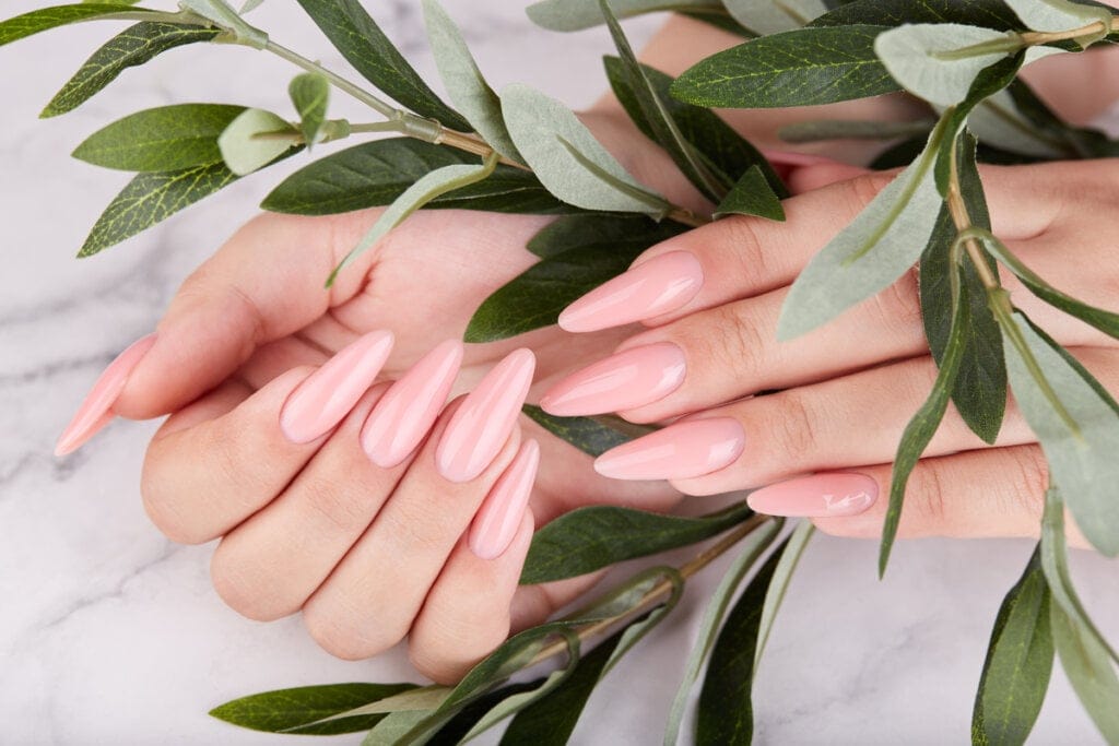 Unhas alongadas pintadas de rosa em cima de plantas