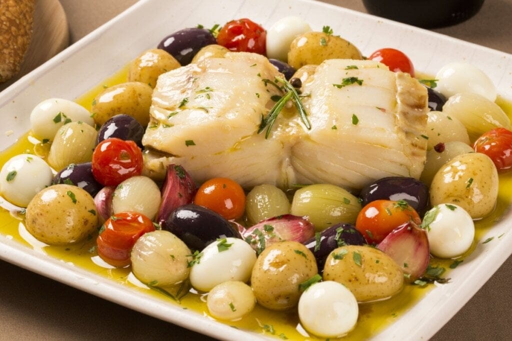 Bacalhau assado servido com legumes em prato fundo branco