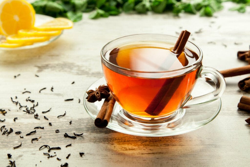Xícara transparente com chá de canela e canela em pau em cima de uma mesa de madeira