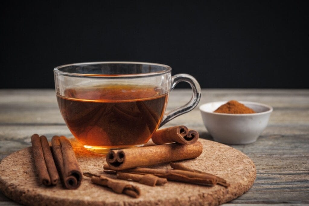 Xícara de vidro com chá de café e canela em cima de uma bandeja redonda e paus de canela ao redor