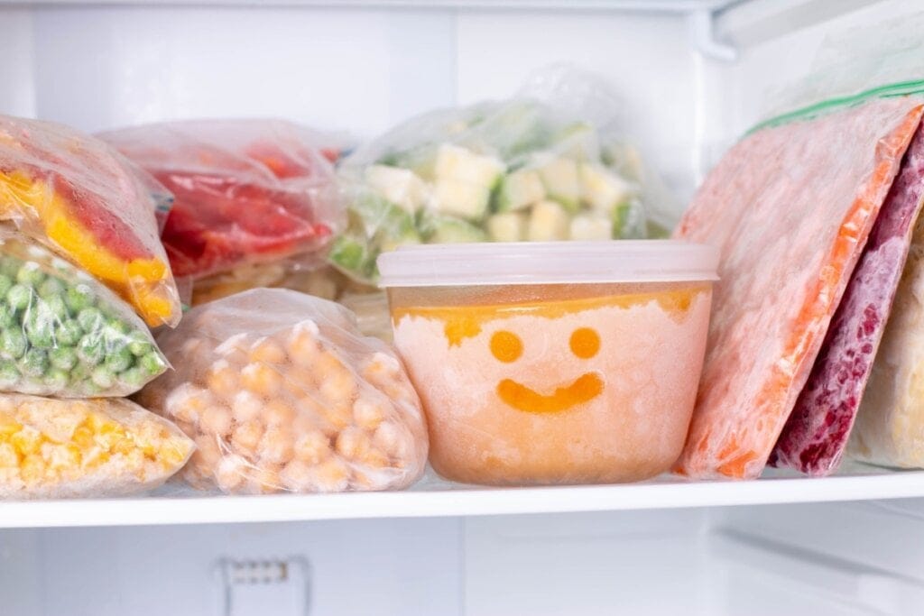 Sacos transparentes e potes com alimentos armazenados no congelador, no pote há um rosto feliz