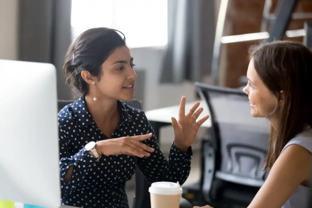 Mulher sentada conversando com outra mulher em uma sala de reuniões 