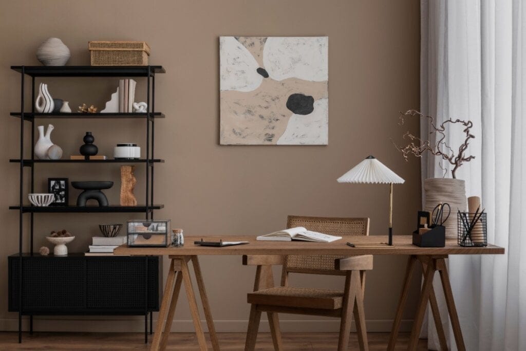 Escritório com decoração em tons neutros, mesa de madeira, cadeira de palhinha e prateleira com objetos decorativos em preto e branco