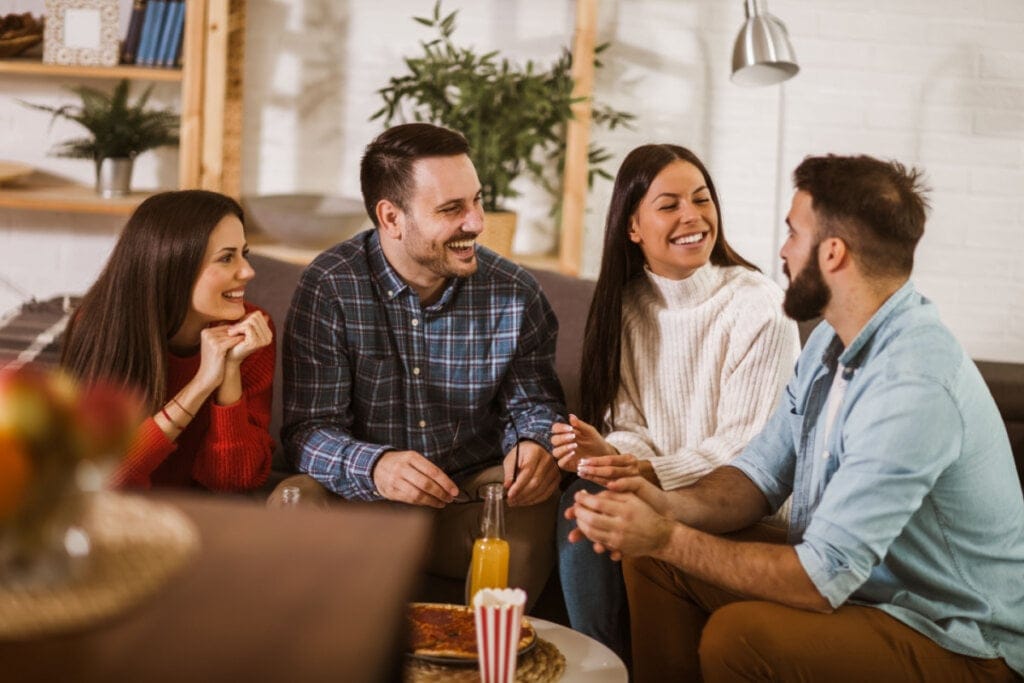 Quatro amigos sentados em um sofá conversando e sorrindo