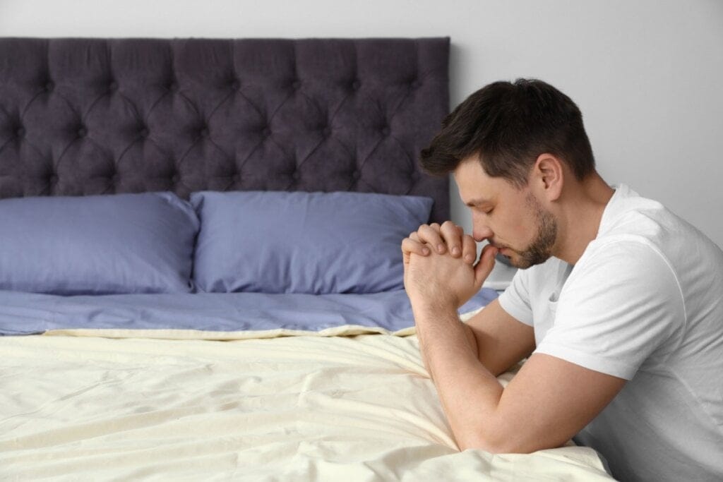 Homem rezando ajoelhado ao lado da cama 