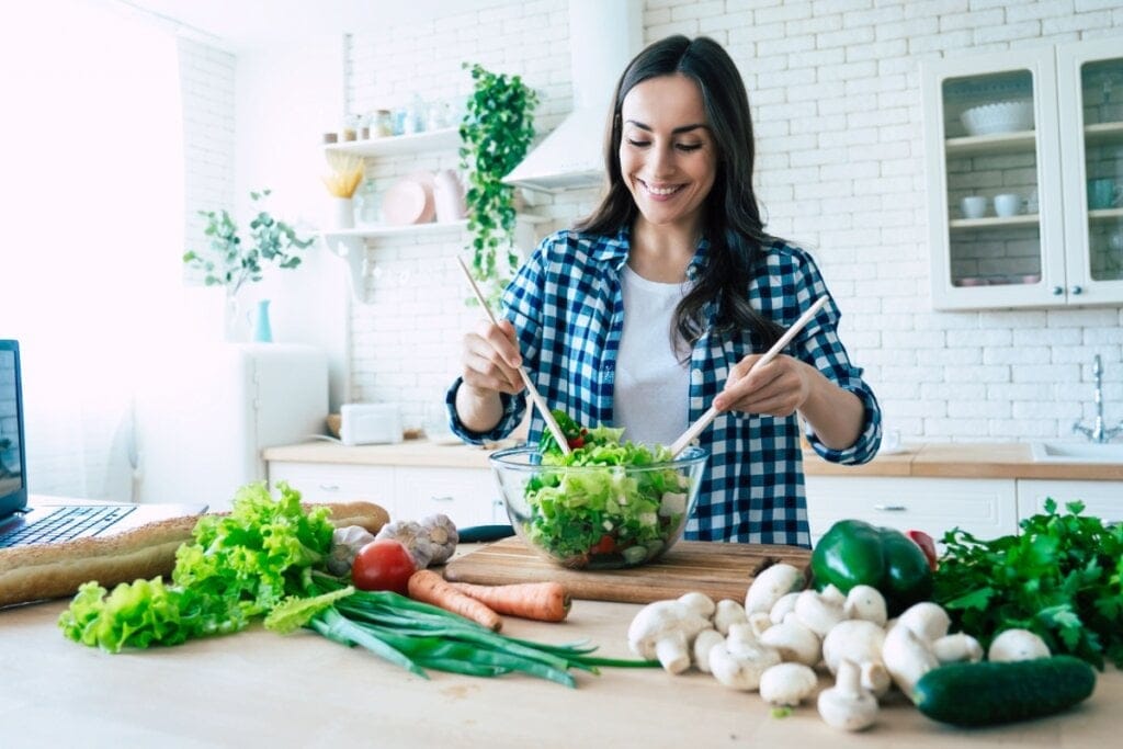 Jovem preparando salada na bancada da cozinha