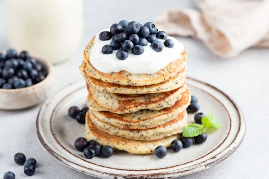 Panquecas com chia empilhadas em um prato branco e decoradas com iogurte e blueberry