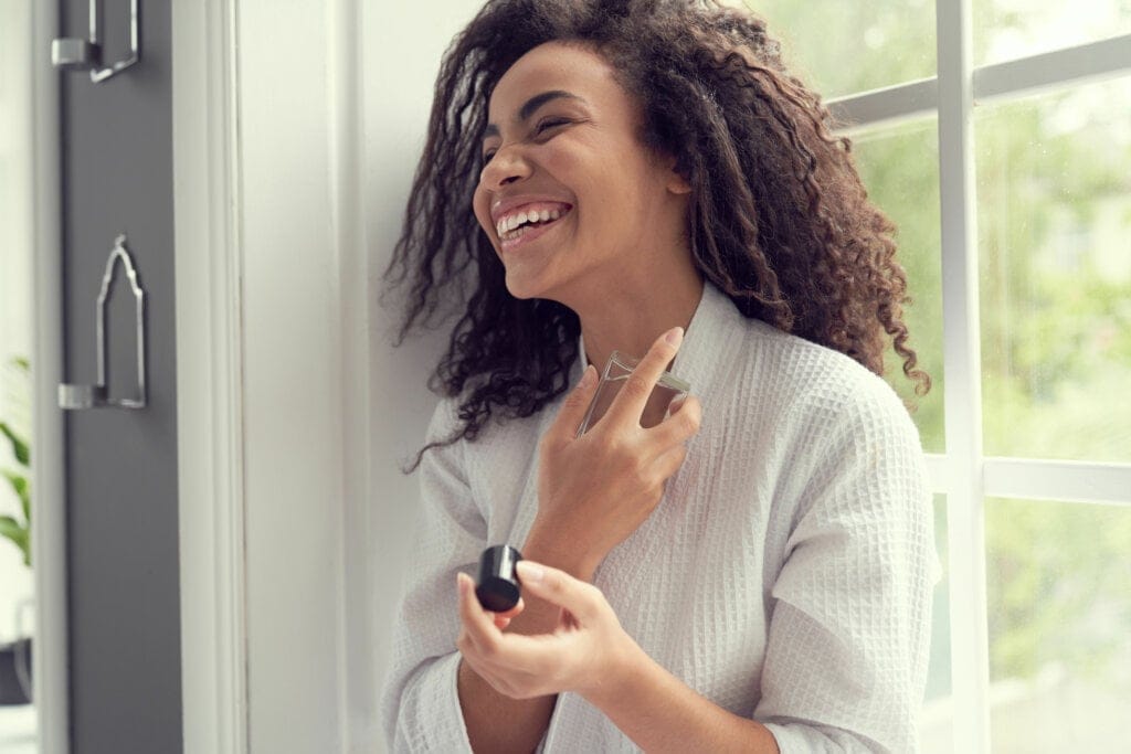 Mulher sorridente passando perfume no pescoço