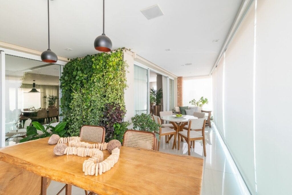 Varanda com tela solar, mesa de madeira e parede com plantas