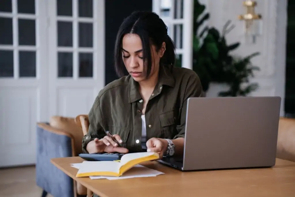 Jovem com cabelo preto e usando camisa social verde fazendo calculo na calculadora e no caderno. 