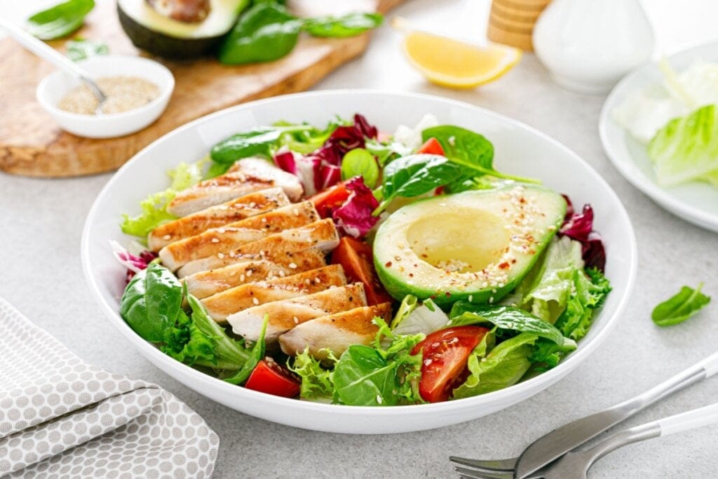 Saladeira branca com folhas, frango fatiado e abacate
