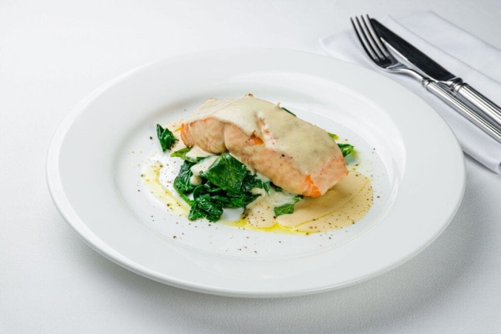 Salmão grelhado servido com molho branco e espinafre 