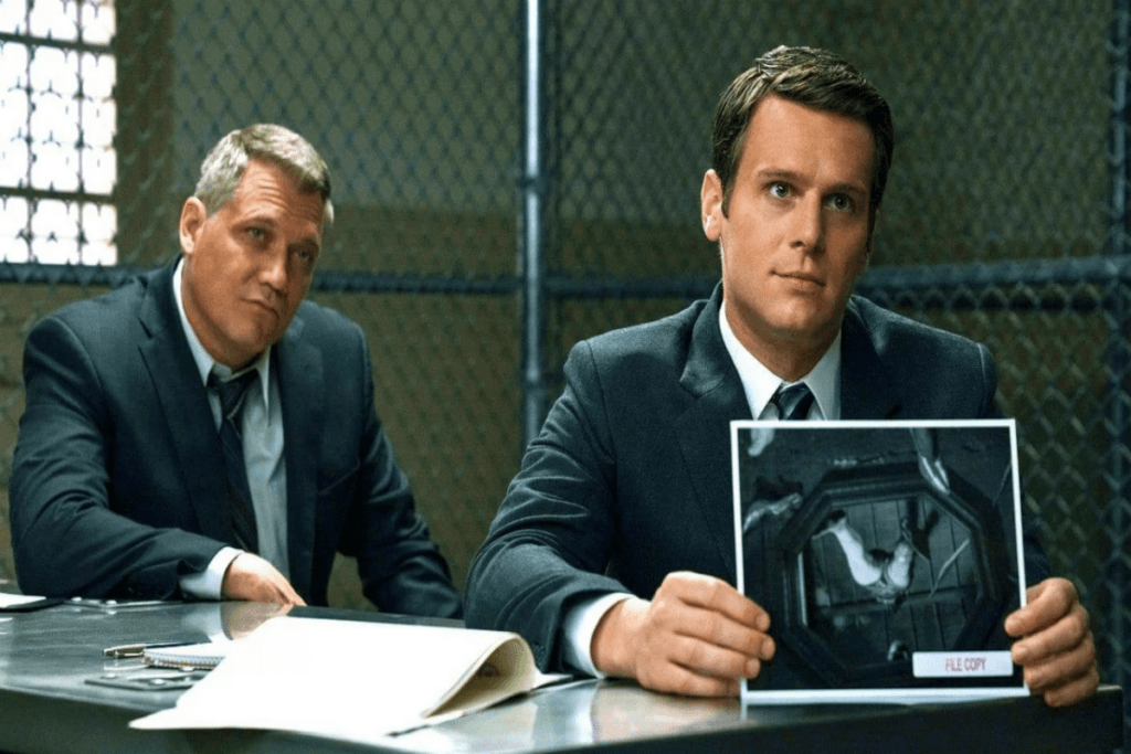 Dois homens de terno sentados e mostrando uma imagem de cena de crime