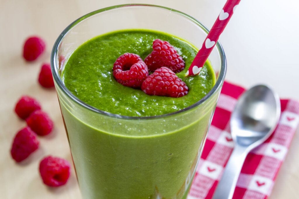 Copo de vidro com suco verde decorado com três framboesas